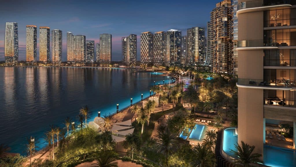 Evening view of Dubai Design District&rsquo;s waterfront residential towers, featuring illuminated high-rises, palm-lined promenades, and private pools adjacent to the canal.