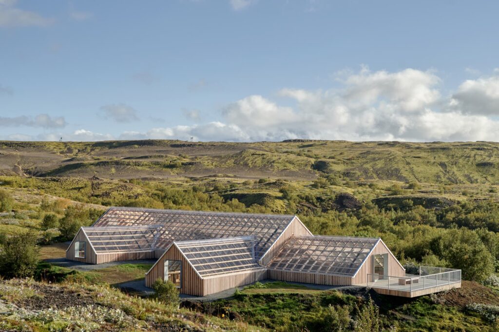 Modern wooden structure with geometric glass roof nestled in Icelandic lava fields under a partly cloudy sky.