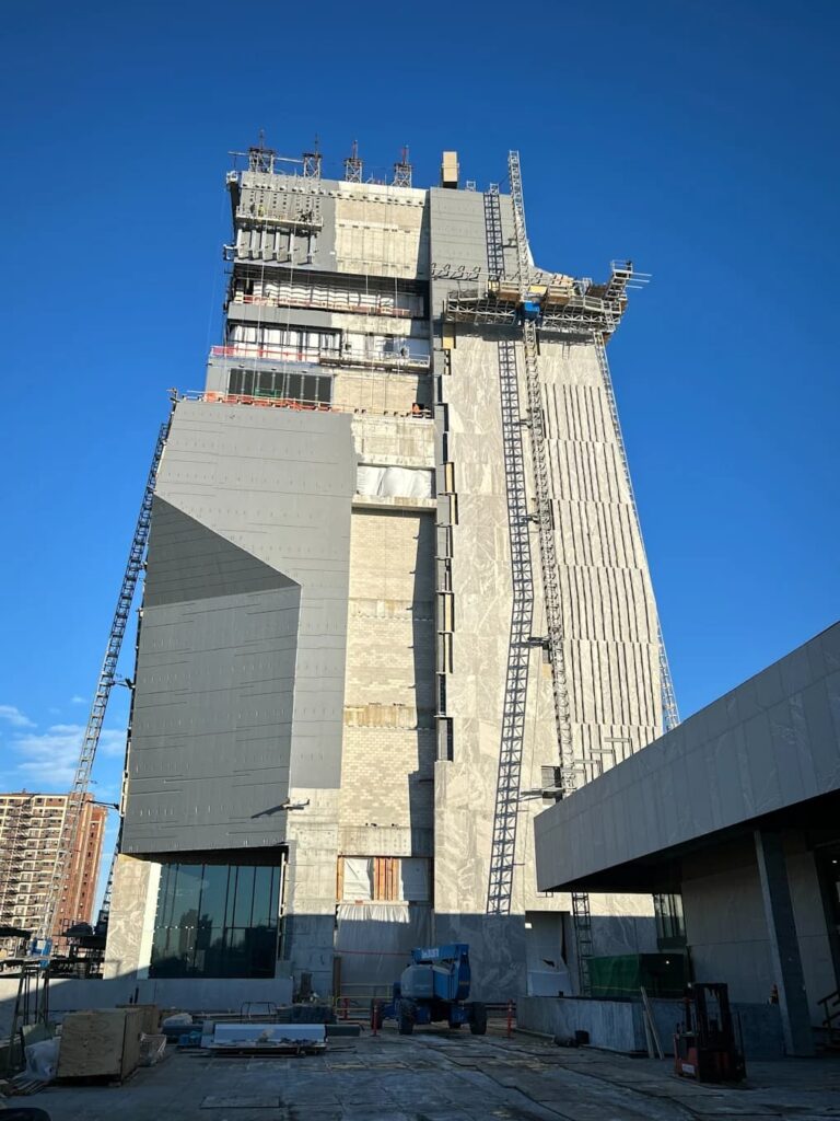 The Obama Presidential Center&rsquo;s 225-foot museum tower rises against a clear blue sky, its concrete and stone facade partially clad as construction progresses.