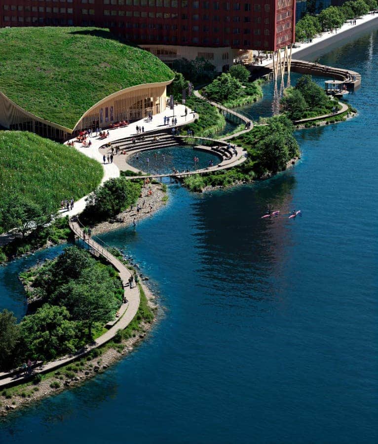 منظر جوي لحديقة درامن النهرية يظهر مظلة ذات سقف أخضر، وطرق متعرجة، ومناطق نشاط على ضفاف النهر متكاملة مع البنية الحضرية.