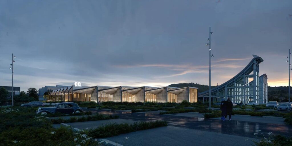 Twilight exterior view of the Michelin Factory Museum in Clermont-Ferrand, illuminated at dusk with warm interior lighting contrasting against the preserved steel and concrete industrial frame, highlighting its adaptive reuse as a cultural landmark.