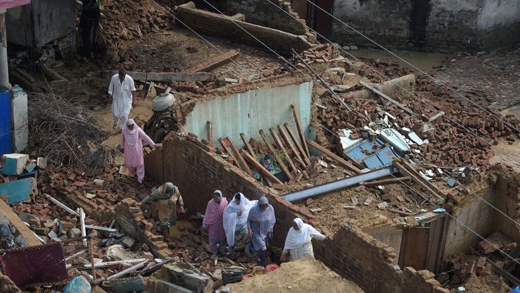 Residents navigate the widespread destruction and rubble of collapsed brick homes in a village.