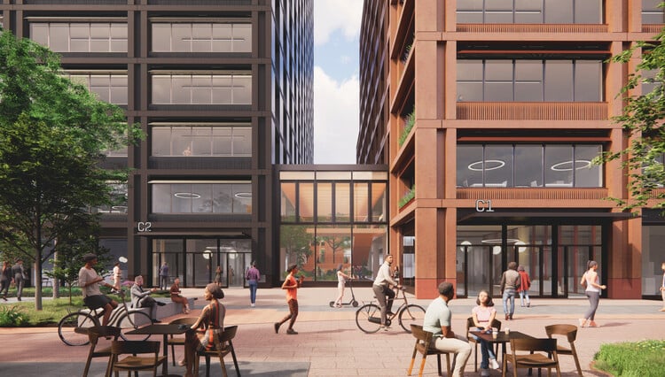 ساحة صديقة للمشاة بين مبنيي C1 وC2 في منطقة سيستر بمانشستر، تضم مقاعد خارجية، دراجات، ومساحات خضراء &mdash; وتُظهر التوسع الحضري من خلال تصميم بشري النطاق وحياة عامة نشطة.