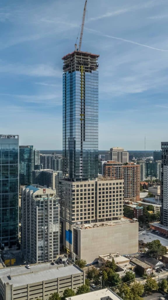 Atlanta mixed-use tower rising above Midtown skyline, its glass facade reflecting surrounding buildings under a clear blue sky.