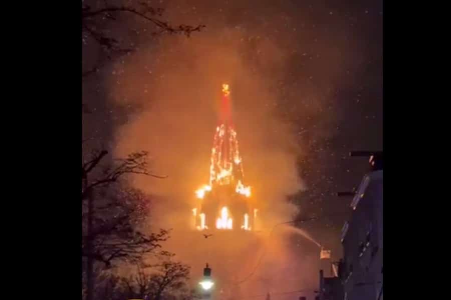 Nighttime view of the Vondelkerk church tower fully engulfed in flames, with smoke rising against the dark sky as firefighters attempt to control the blaze.