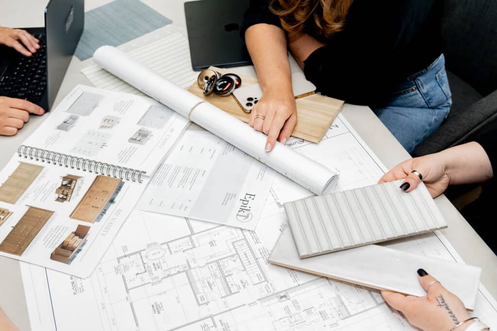 لقطة قريبة لمعماريين يراجعون مخططات الأرضيات وعينات المواد وكتالوجات التصميم خلال جلسة استراتيجية داخلية في شهر يناير.