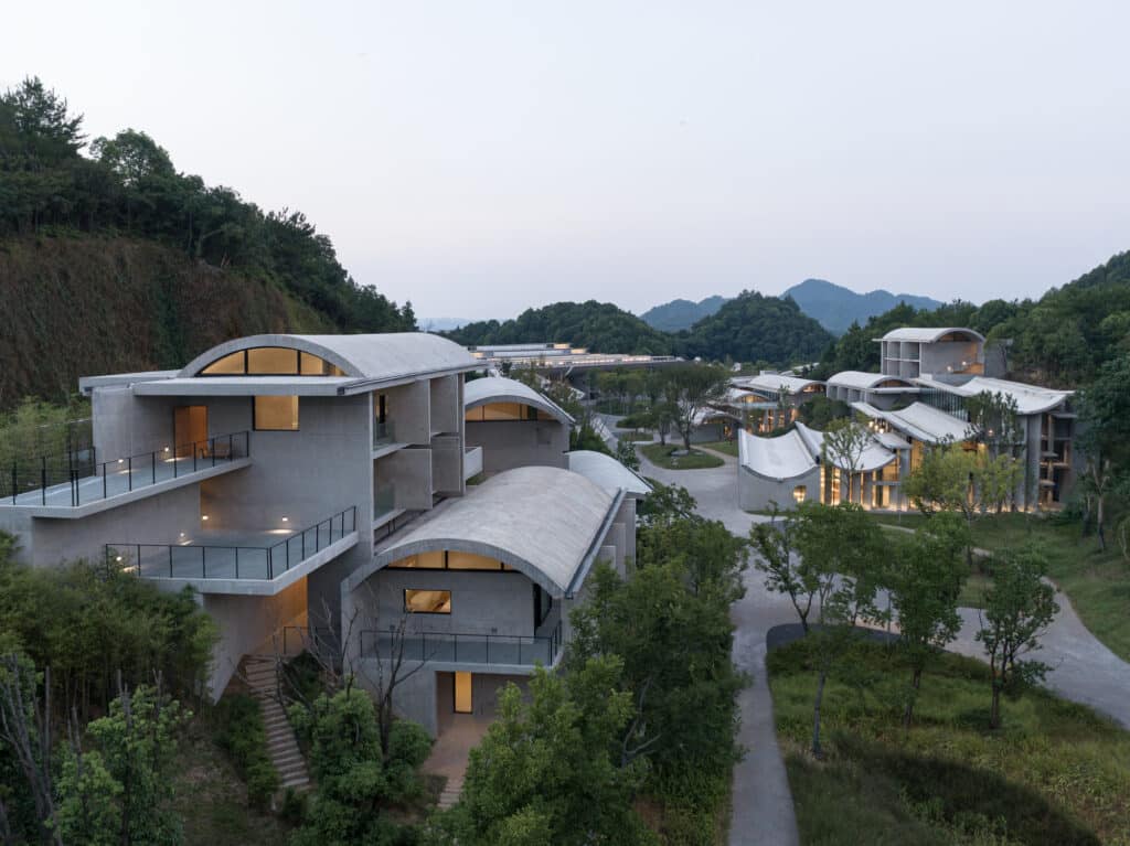 An evening view of the Zijing International Conference Camp by Zhu Pei, with its collection of buildings featuring gracefully curved roofs nestled in a green valley, representing a poetic [Poetic Architecture].
