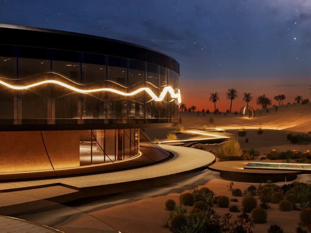 Clio House at night: illuminated circular pavilion with glowing wave-like facade and desert pathways under starry sky in Dubai&rsquo;s Margham Desert.