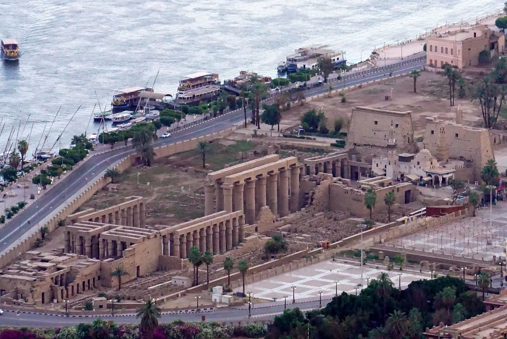 Panoramic view of Luxor Temple from the Nile showing Pharaonic colonnades, Abu Al-Haggag Mosque, and riverfront, highlighting urban and architectural continuity.