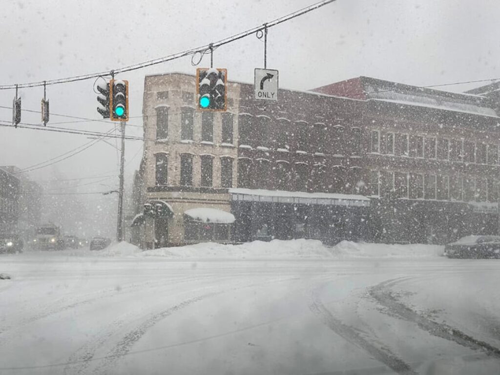 Stranded travelers inside an airport terminal look out at a snow-covered airfield, illustrating the fragility of aviation infrastructure during Storm 2026.