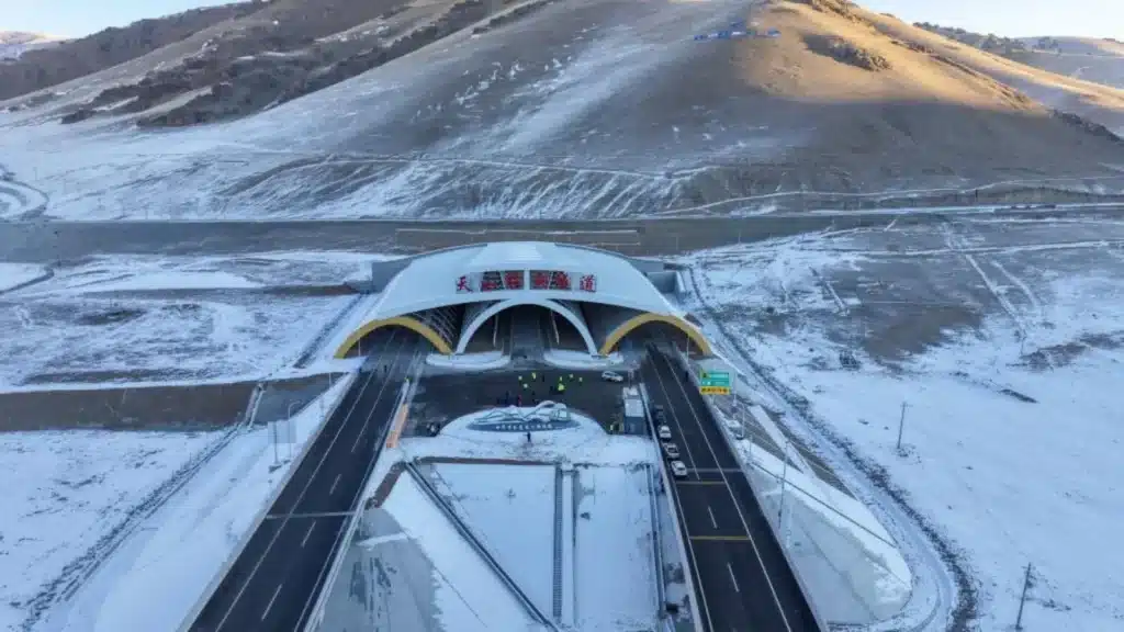 Aerial view of the Tianshan Shengli Tunnel entrance nestled in a snow-dusted mountain range, with its arched canopy and bilingual signage visible under morning light. Structural Stabilization