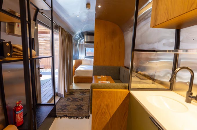 منظر داخلي لوحدة نوماد كلباء، يظهر تغليفًا خشبيًا، ومطبخًا صغيرًا، وأبواب زجاجية تفتح على شرفة خاصة &mdash; إعادة الاستخدام البيئي في كفاءة المساحة.