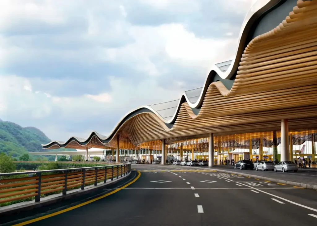 منظر خارجي لمحطة مطار جادوكدو الجديد بواجهة خشبية متعرجة وسقف منحني، أمام خلفية جبلية ساحلية.