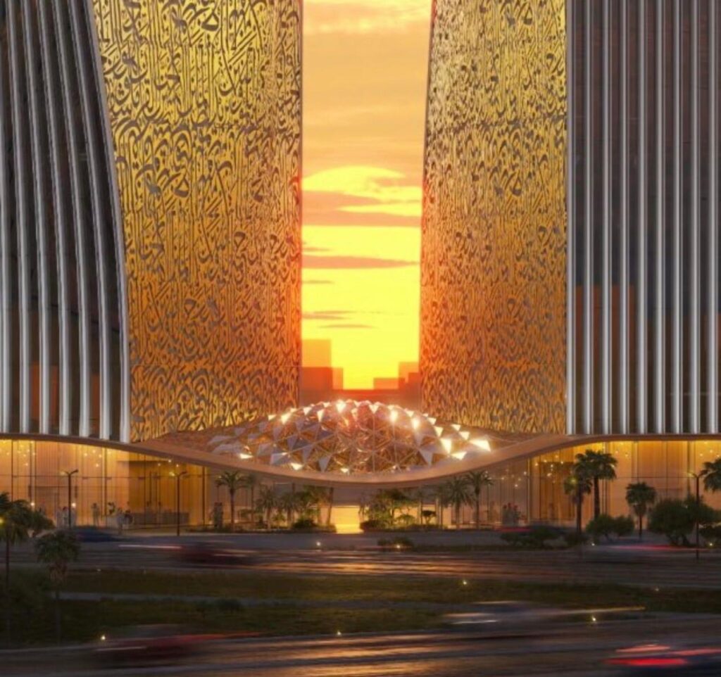 Reflective plaza surface at sunset framed by monumental arch with Arabic calligraphy, overlooking Riyadh skyline.
