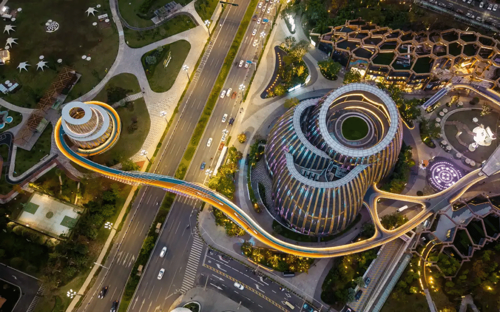 Top down aerial view of the uniquely spiraled Digital Art Museum at the Yibin High Speed Railway Station development, connected by a glowing pedestrian bridge at night