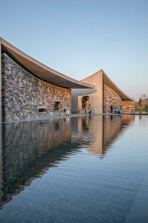 The stone and concrete facade of the Jingdezhen Imperial Kiln Museum reflected in the tranquil water of a surrounding pool at sunset.