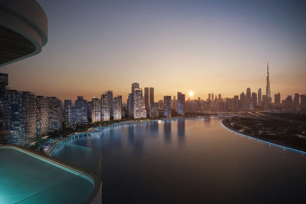 المخطط السكني ومنظر غروب الشمس من شرفة سكنية تطل على أبراج دبي ديزاين ديستريكت على الواجهة المائية وسماء برج خليفة، ويُبرز دمج الحياة الفاخرة مع الحجم الحضري.