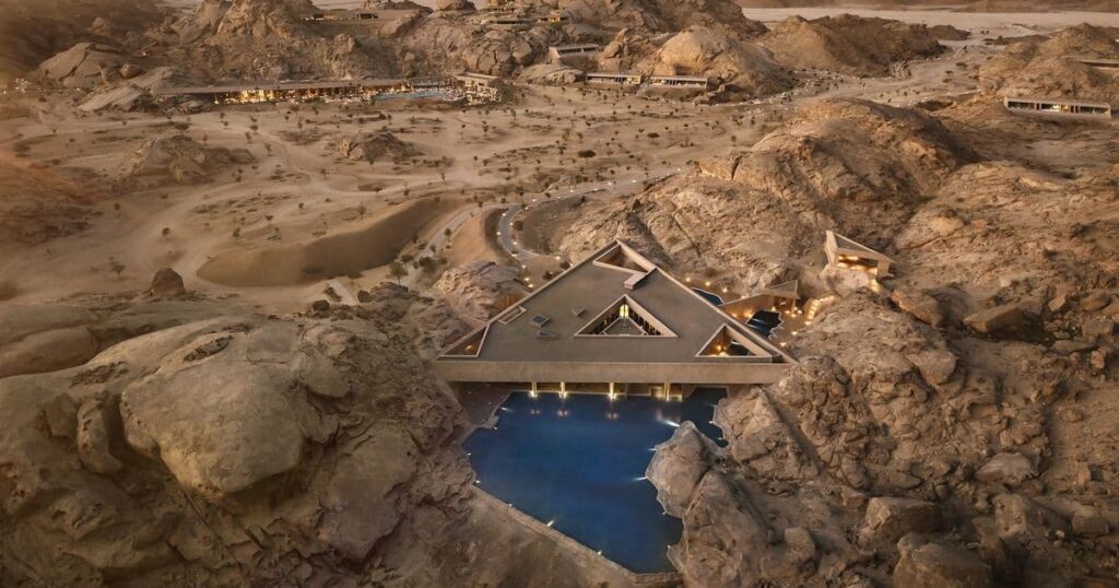 Architectural Design Aerial view of a geometric luxury resort nestled in a rocky desert landscape, featuring a triangular building over a pool at dusk.