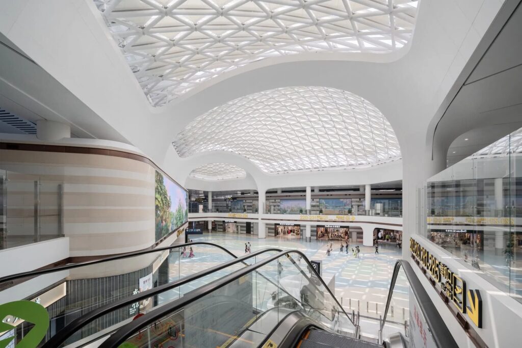 Atrium of Yantai Terminal 2 with glazed diagrid dome, escalators, and retail zones. Daylight filters through the lattice ceiling, enhancing spatial clarity.