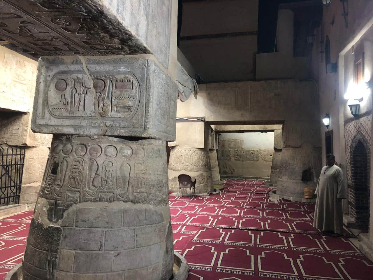 Interior of Abu Al-Haggag Mosque with carved Pharaonic columns featuring Ma’at symbols and prayer rugs, showing layered sacred architecture.