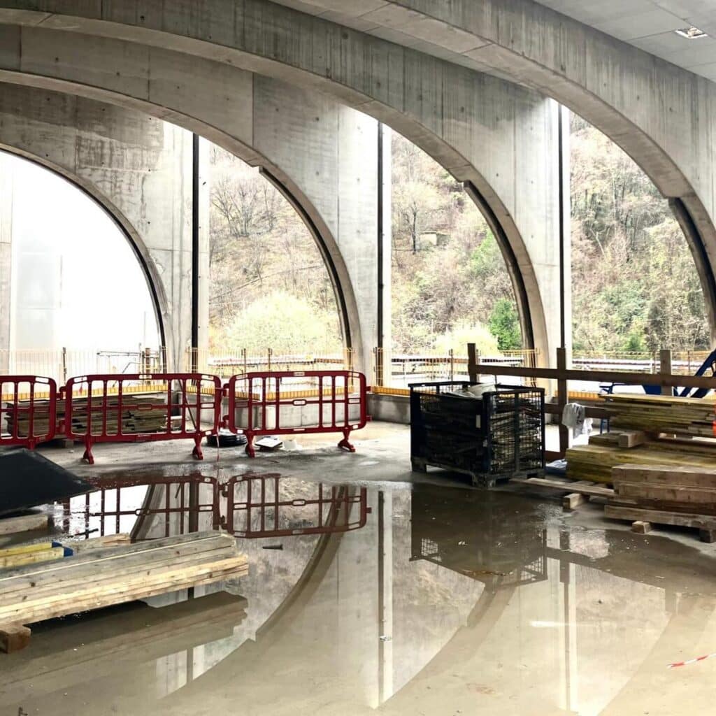 Interior view of San Pellegrino Future Factory under construction, showing concrete arches framing forested valley landscape