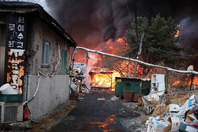 Narrow alley in Guryong Village during the January 2026   , showing burning structures, debris, and makeshift homes with flammable cladding  a direct consequence of absent fire safety regulations and urban neglect.