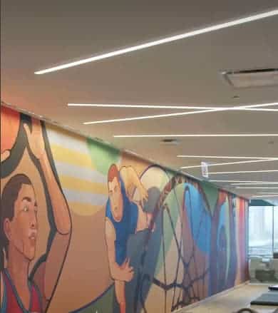 منظر داخلي لممر طويل يضم جدارية ملونة تصور رياضيين في حركة، ومضاءة بإنارة خطية من السقف.