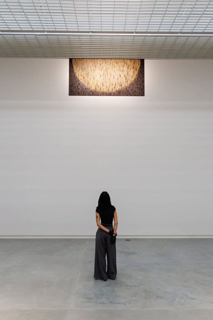 زائر يشاهد عملًا فنيًا كبير الحجم في قاعة عرض بسيطة