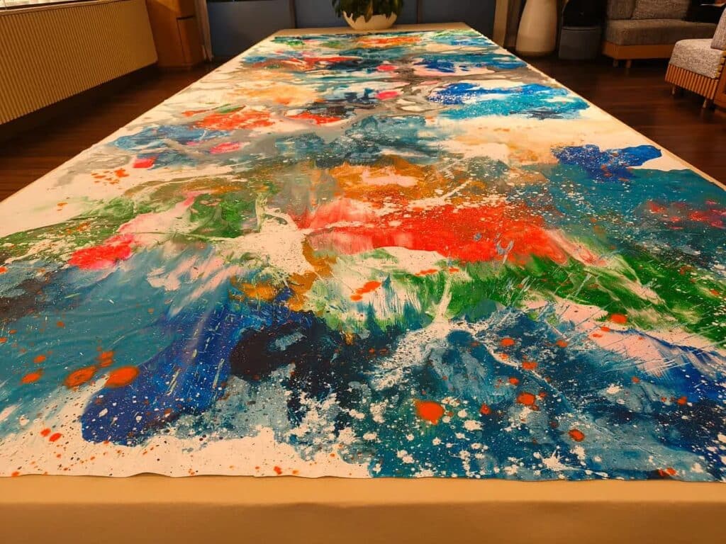 Large abstract painting with vibrant blue, red, and green brushstrokes displayed on a long table in a modern interior setting.