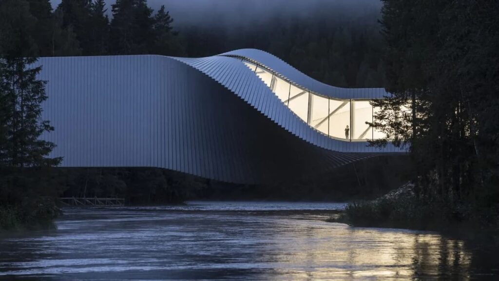 الاستدامة المعمارية في الشكل  مبنى تويست في متحف كيستيفوس، النرويج، يقطع نهرًا بحجمه الأبيض المتعرج، مضيئًا أمام خلفية الغابة.