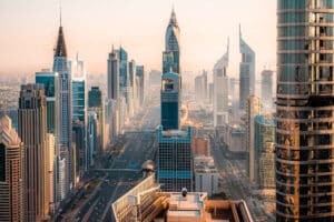 A high-angle view of the Sheikh Zayed Road in Dubai featuring iconic skyscrapers, the metro line, and urban traffic during golden hour.