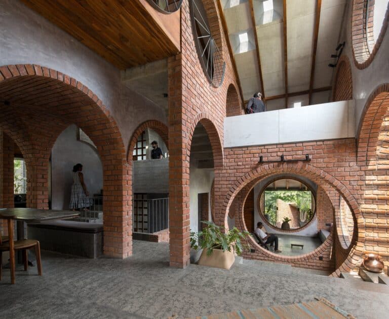Interior of Solapur multi-generational house featuring exposed brick arches, circular openings, and grey stone flooring under natural light.