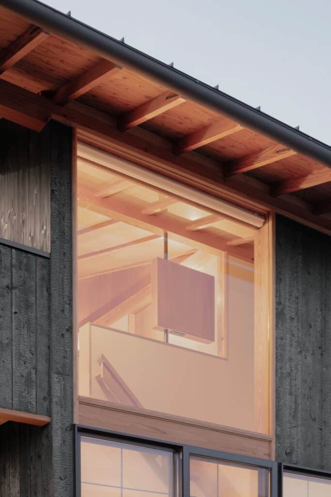 Close-up of a large upper-floor window at dusk, reflecting the internal timber ceiling and a hanging cabinet.