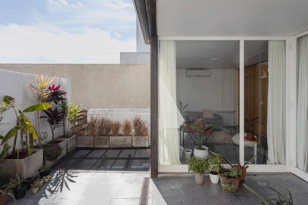 Outdoor private terrace of a PH unit apartment with grey floor tiles, potted plants, and a glass wall connecting to the interior living space.