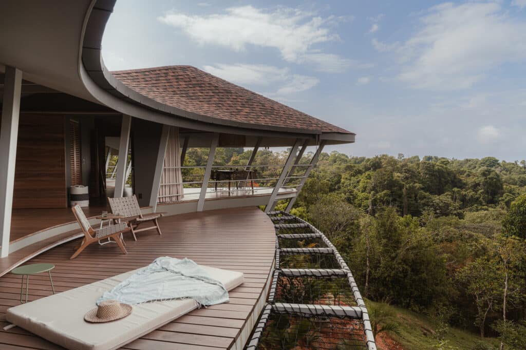 Wide outdoor wooden deck of Ojo de Nila house featuring lounge chairs and a view of the dense rainforest.