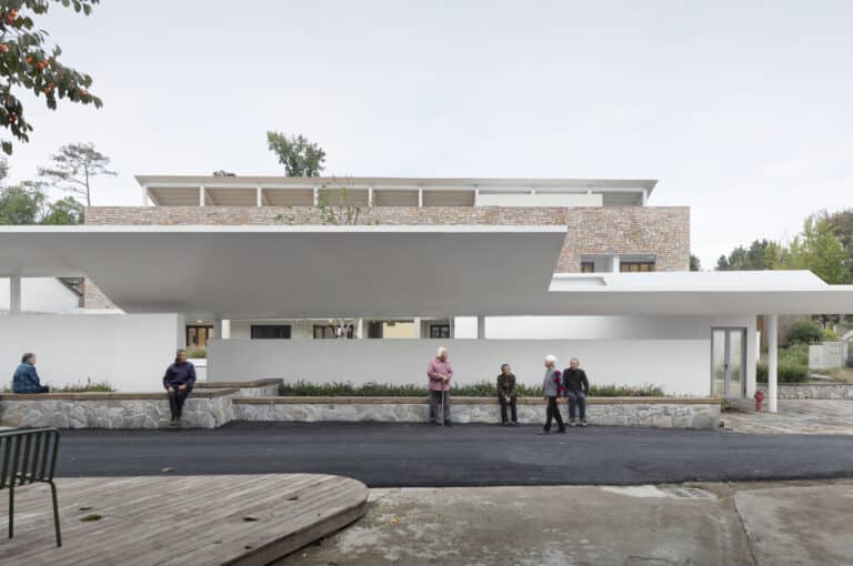 Local villagers sitting on stone benches under the long white eaves of Qingyi Lodge.