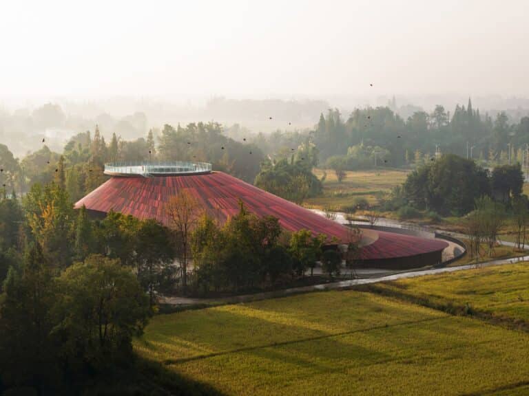 Aerial view of Douban Museum in Sichuan showing the red bean-shaped roof nestled within the traditional Linpan greenery.