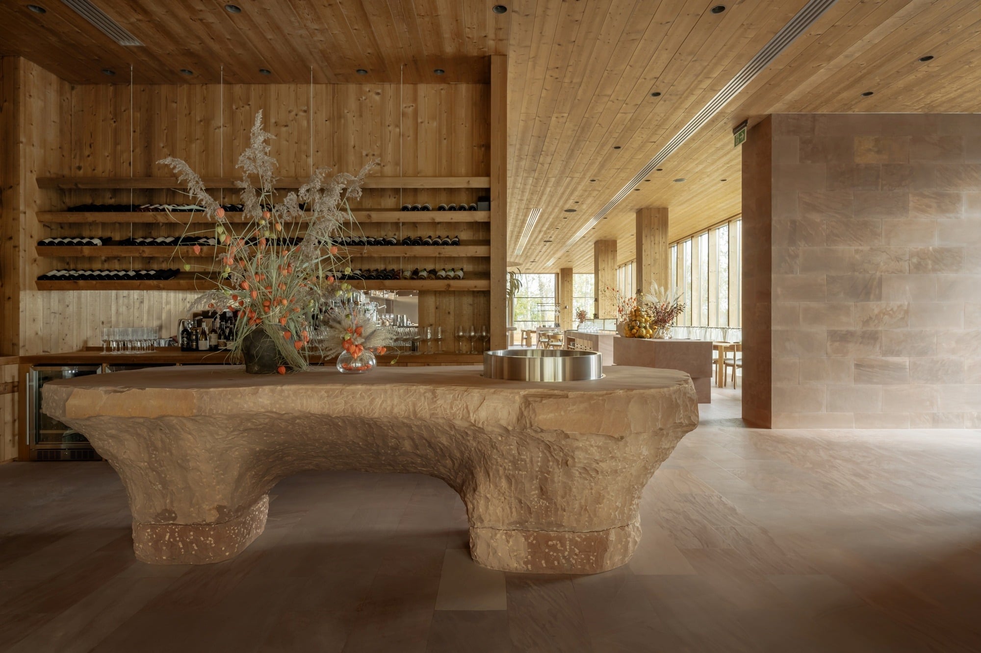 A sculptural monolithic stone service counter in the interior of Seven Lakes restaurant with wooden walls and wine shelves.