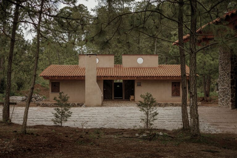 Symmetrical facade of a modern forest cabin in Tapalpa with terracotta walls and a tiled roof, surrounded by pine trees.
