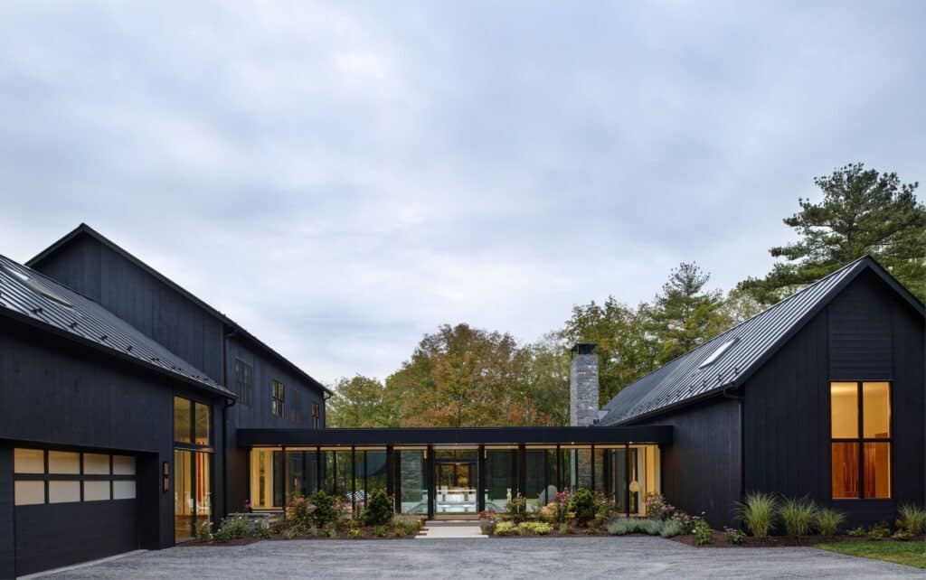 Exterior facade of WACE House featuring black vertical timber cladding and a glass connecting bridge.