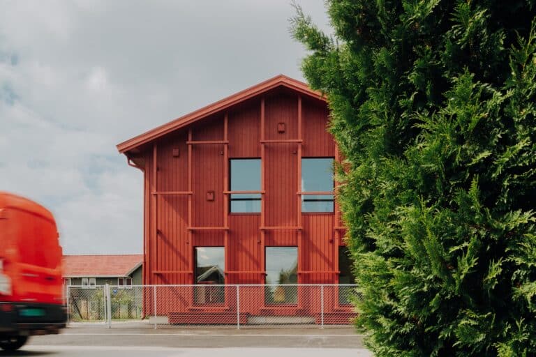 Exterior view of Alvim Kindergarten's new two-story extension featuring red vertical wooden cladding and a decorative trellis in Sarpsborg, Norway.
