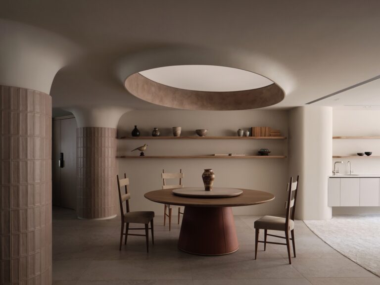 Round wooden dining table under a circular ceiling cove in C.S.C Residence with textured pillar details.