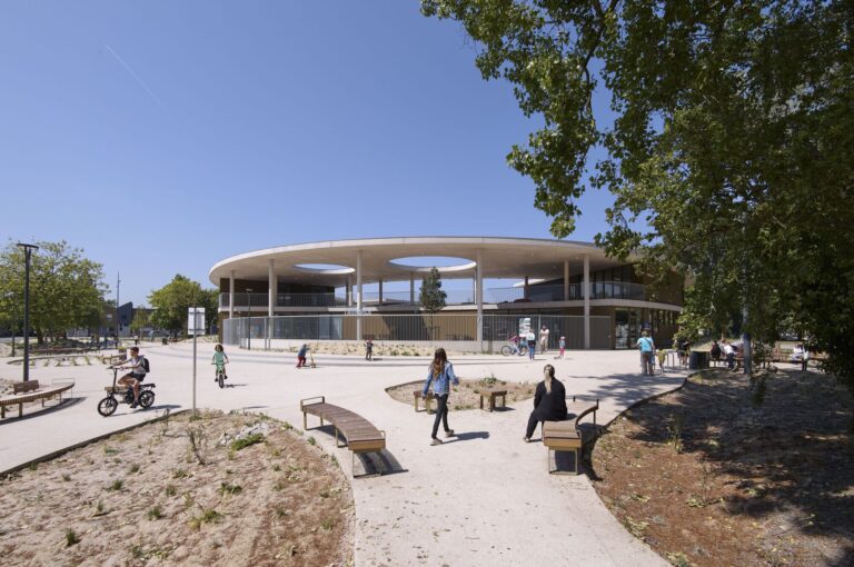 External view of L'Alliance school complex in Dunkerque showing the circular concrete canopy and public plaza with children playing.