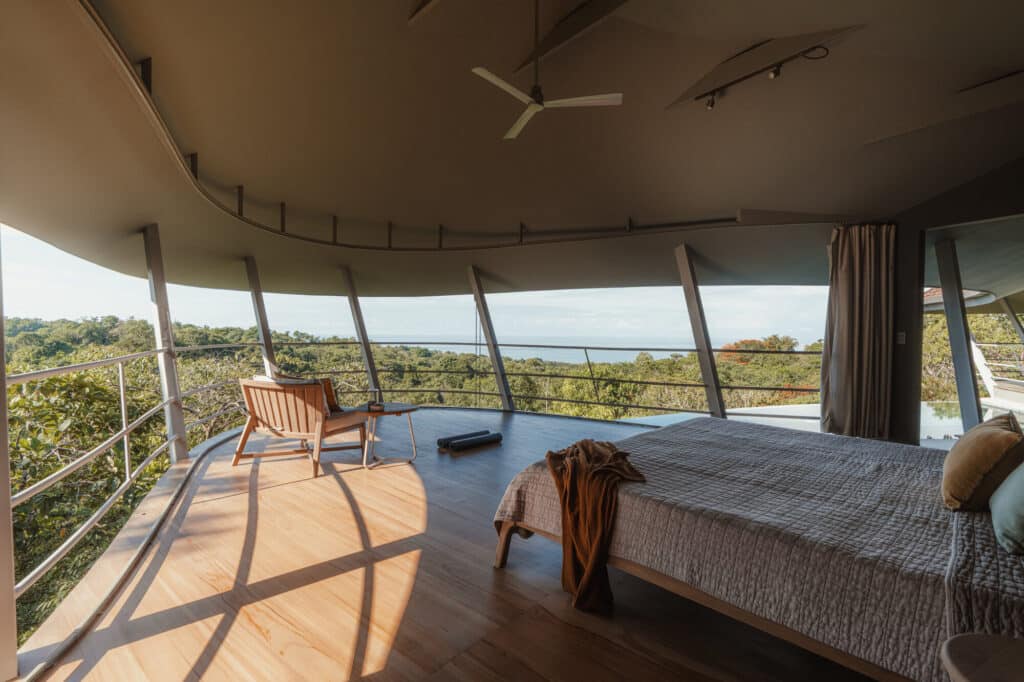 Interior of a bedroom in Ojo de Nila house with open walls facing the Pacific Ocean and natural wood flooring.
