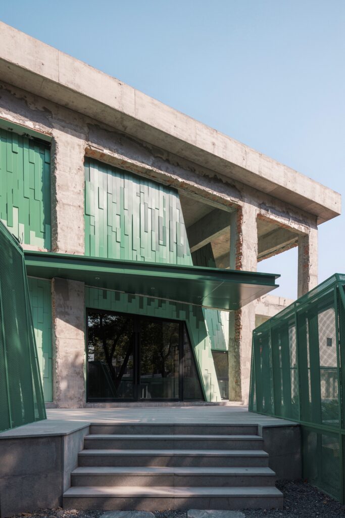 Main entrance of Xingguang Theater featuring green tiered metal panels under a raw industrial concrete structure.