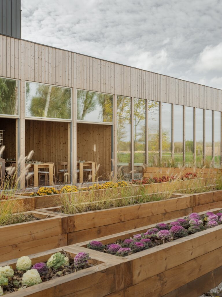 Exterior view of Seven Lakes project featuring wooden building facade and raised timber garden beds with colorful plants.