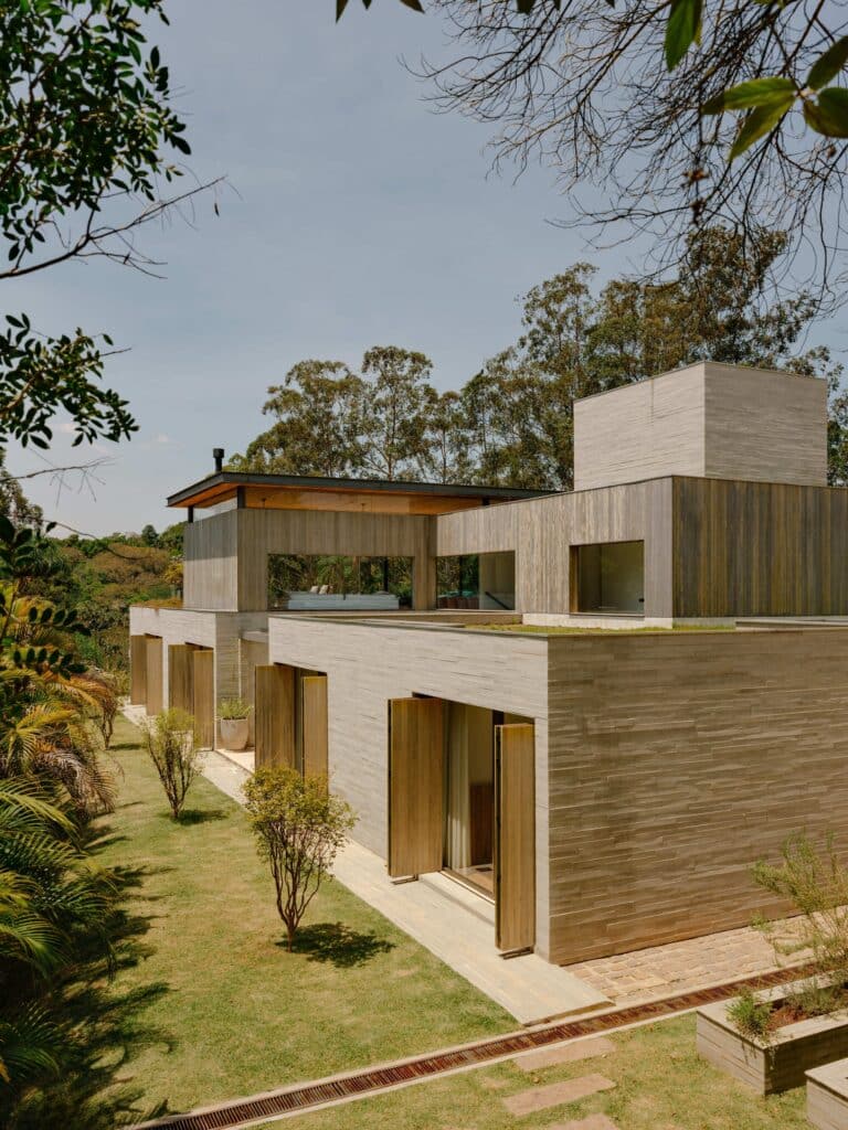 Exterior view of the stacked concrete and wood volumes of Casa CR JL showing the garden and sloped site.