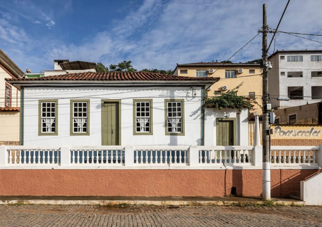 Front facade of Heloisa and Leonardo House featuring traditional white walls, green wooden doors, and windows in a colonial architectural style.