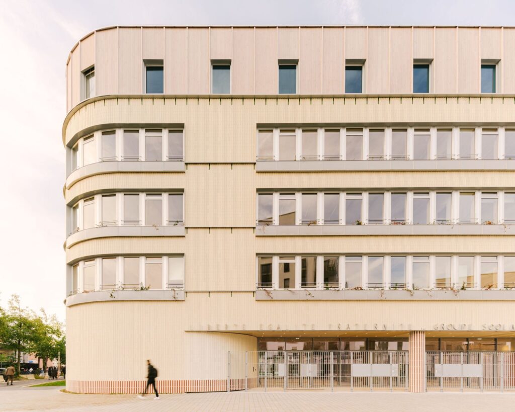 Main street facade of Dominique Frelaut school featuring light-colored vertical brickwork and curved corners.