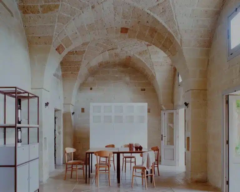 Interior of a renovated stone farmhouse in Salento featuring cross-vaulted ceilings and a modern white tufaceous stone divider.